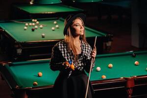 une fille dans une chapeau dans une billard club avec une queue dans sa mains.billard Jeu photo