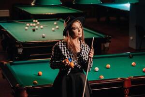 une fille dans une chapeau dans une billard club avec une queue dans sa mains.billard Jeu photo