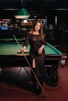 une fille dans une chapeau dans une billard club avec une queue dans sa mains.piscine Jeu photo