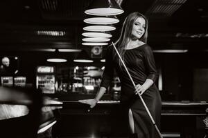 une fille dans une chapeau dans une billard club avec une queue dans sa mains.billard jeu.noir et blanc photo