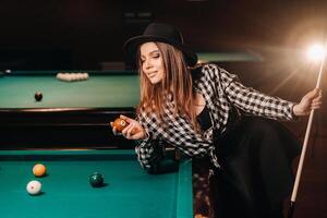 une fille dans une chapeau dans une billard club avec une queue et des balles dans sa mains.jouer bassin photo