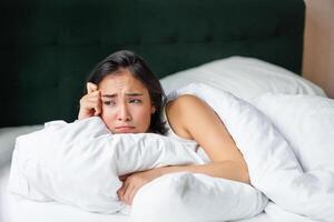 triste et sombre asiatique fille mensonge dans sa lit, grimaçant et pleurs, sentiment bouleversé, dépenses temps dans sa chambre à coucher, étreindre oreiller photo