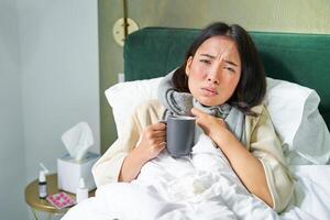portrait de couché asiatique fille dans lit, sentiment malade, contagieux du froid et rester à maison, à la recherche mauvais pour la santé, en buvant chaud thé photo