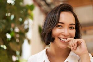 proche en haut portrait de magnifique brunette asiatique fille, souriant et à la recherche affectueux à caméra, glousser mignonne photo