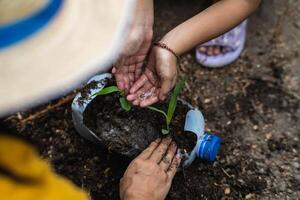 peu fille et maman grandir les plantes dans des pots de recyclé l'eau bouteilles dans le cour. recycler l'eau bouteille pot, jardinage Activités pour les enfants. recyclage de Plastique déchets photo