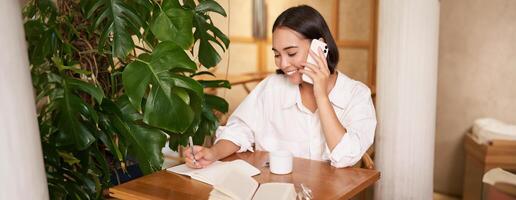 souriant femme parlant sur mobile, répondre téléphone appel et à la recherche content, séance dans café photo