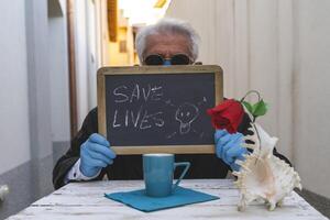 adulte homme avec masque séance à une table est montrant une positif message photo