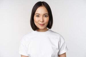 proche en haut portrait de Jeune asiatique femme à la recherche à caméra, portant T-shirt, souriant et à la recherche content, blanc Contexte photo