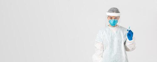 COVID-19 [feminine, coronavirus maladie, soins de santé ouvriers concept. l'air sérieux sur de soi asiatique femelle médecin dans médical respirateur et personnel protecteur équipement, en portant seringue avec vaccin photo