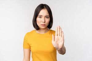 portrait de asiatique femme à la recherche sérieux et en colère, montrant Arrêtez interdire geste, tabou signe, interdiction qch, permanent dans Jaune T-shirt plus de blanc Contexte photo