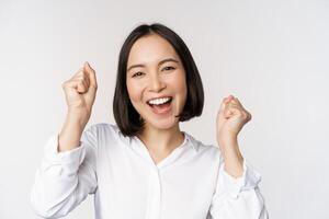 proche en haut visage portrait de dansant asiatique femme souriant, triomphant et célébrer avec content émotion, permanent plus de blanc Contexte photo