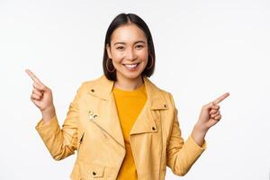 content magnifique asiatique fille montrer du doigt les doigts la gauche et droite, montrant bannière logo, démontrant vente, permanent dans Jaune veste plus de blanc Contexte photo