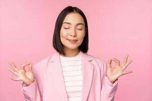 garder calme. souriant Jeune asiatique femme méditer, entraine toi yoga, pleine conscience et relaxation à travail, haleine, inhaler air avec heureux affronter, permanent plus de rose Contexte photo