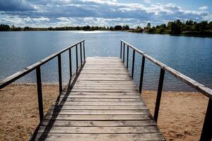 en bois jetée par le bleu clair eau, entouré par forêt sur une ensoleillé journée. solaire éblouissement sur le l'eau. Extérieur des loisirs par le lac. photo