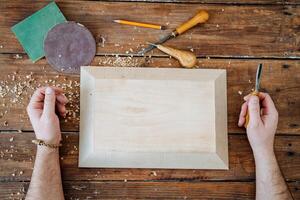 le charpentier mains mensonge sur une table dans le atelier. blanc planche pour bois sculpture. préparation avec travail avec bois photo