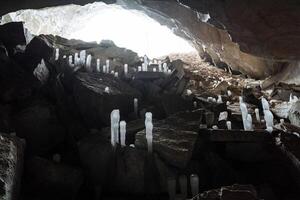 la glace stalactite la grotte froid. stalagmile dans le la grotte dans l'hiver. le glacé Royaume de le donjon. blanc lumière dans une foncé grotte. entrée à une grand fosse souterrain. photo