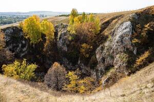 vue de au dessus de le rocheux falaise et le entrée à le grotte, des arbres grandir sur le rochers, le feuillage a tourné Jaune. magnifique Montagne paysage photo