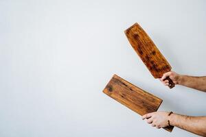 mains tenir Coupe planches contre le Contexte de une blanc mur. deux en bois objets dans le mains de une Jeune homme. ustensiles de cuisine. minimalisme photo