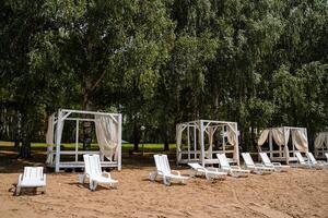 blanc Soleil chaises longues et tentes pour relaxant sur le sablonneux vide plage. du repos par le l'eau sur une ensoleillé été journée. photo