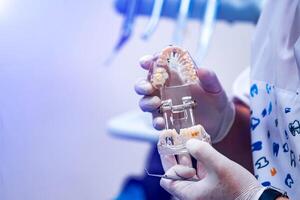 médecin spectacles sur une Plastique mâchoire échantillon ou modèle différent méthodes de les dents traitement. moderne dentaire clinique Contexte. santé concept. blanc médical gants sur Masculin médecins mains. photo