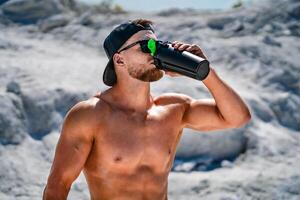 portrait de une Beau à moitié nu bodybuilder homme sur une Montagne avec une bouteille de l'eau. photo