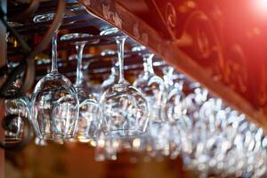 fermer de certains nettoyer du vin des lunettes accroché sur le bar à une restaurant plus de le flou Contexte avec rouge lumière fuites. des lunettes préparé pour une fête à le bar. photo