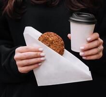 femme en portant une agresser de café et flocons d'avoine biscuits dans sa mains dans café magasin photo