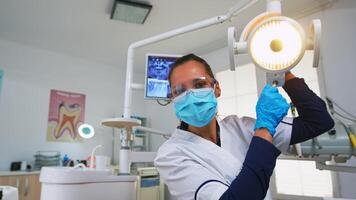 patient pov dans dentaire chaise fabrication performant périodique les dents vérifier dans moderne stomatologique clinique. dentisterie médecin éclairage le lampe et examiner la personne portant protection masque et lunettes. photo