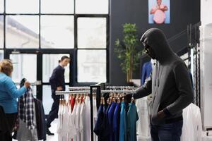 africain américain voleur en essayant à voler décontractée porter, à la recherche autour à voir si Quelqu'un en train de regarder lui. voleur voler Vêtements magasin, portant capuche et des lunettes de soleil tandis que vol accessoires. la criminalité concept photo