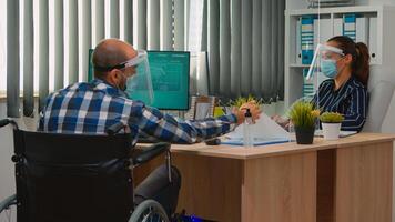 paralysé financier ouvrier dans fauteuil roulant avec protection masque travail dans Nouveau Ordinaire affaires Bureau parlant avec collègue. immobilisé pigiste dans entreprise entreprise respectant social distance. photo