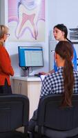 Jeune Dame visite stomatologique clinique pour les dents vérification tandis que dentisterie médecin en train de préparer vieux homme pour dentaire chirurgie dans Contexte. les patients séance dans bondé attendre pièce de orthodontiste Bureau photo