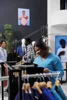 africain américain Shopaholic femme achats pour décontractée porter dans moderne boutique, vérification marchandise tissu. élégant client vouloir à acheter Nouveau mode collection dans Vêtements boutique photo