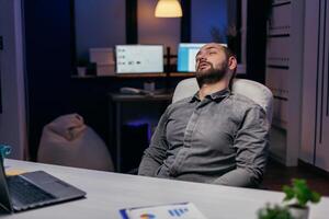 Jeune homme d'affaire repos sur chaise tandis que travail sur date limite. bourreau de travail employé chute endormi car de tandis que travail en retard à nuit seul dans le Bureau pour important entreprise projet. photo