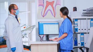 médecin demander assistant à propos suivant rendez-vous tandis que examiner vieux patient dans consultation chambre. les patients séance sur chaises dans attendre zone de bondé professionnel orthodontiste bureau. photo