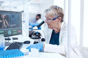 Sénior scientifique en cours d'analyse échantillon de génétique Matériel en utilisant microscope et africain collaborateur dans le Contexte. personnes âgées chercheur porter en dehors scientifique recherche dans une stérile laboratoire avec une moderne technologie. photo