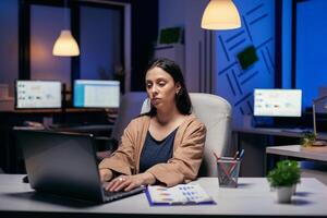 Jeune femme travail sur le portable Faire heures supplémentaires à terminer une date limite séance à sa lieu de travail. intelligent femme séance à sa lieu de travail dans le cours de en retard nuit heures Faire sa emploi. photo