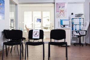 attendre pièce dans clinique avec personne dans il, de face Bureau avec Nouveau Ordinaire ayant signe sur chaise pour social distance dans coronavirus pandémie. vide stomatologie accueil pendant covid-19 épidémie. photo