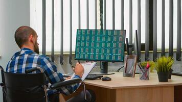 désactivée homme d'affaire séance dans fauteuil roulant immobilisé vérification financier économie Les données prise Remarques dans affaires Bureau discuter avec collègue. handicapé pigiste en utilisant moderne technologie. photo