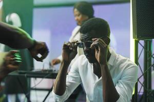 Jeune africain américain homme portant des lunettes de soleil tandis que séance dans boîte de nuit. clubber en mettant sur des lunettes tandis que assister disco fête avec vivre électronique la musique et profiter vie nocturne activité photo