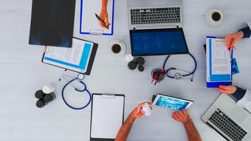 Haut vue de équipe médecins sur bureau table avec stéthoscope et numérique dispositifs ayant conférence. médical groupe travail dans clinique sur copie espace, plat allonger en utilisant moderne technologie. photo