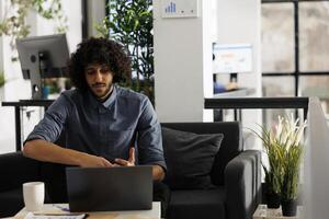 Jeune arabe entrepreneur vérification affaires présentation sur portable dans cotravail espace. exécutif directeur en cours d'analyse entreprise financier rapport tandis que travail dans début en haut Bureau photo