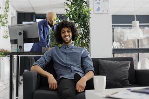 souriant réussi arabe début en haut entreprise entrepreneur dans affaires Bureau portrait. Jeune Beau exécutif directeur à la recherche à caméra, séance sur canapé dans vert cotravail espace photo