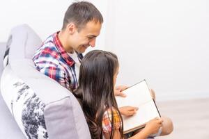 une Jeune père avec le sien peu fille lit le Bible photo