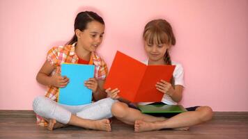 charmant peu les filles sont en train de lire une livre. le concept de éducation. isolé sur rose Contexte photo