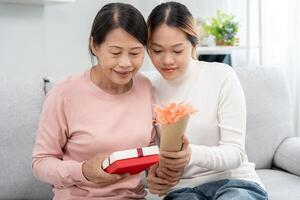 mère jour, mignonne asiatique adolescent fille donner cadeau boîte à mature milieu âge maman. aimer, baiser, se soucier, content sourire prendre plaisir famille temps. célébrer spécial occasion, content anniversaire, content Nouveau années, joyeux Noël photo