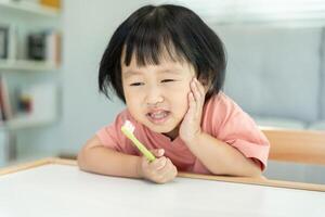 peu asiatique fille presses main à joue, souffre de douleur dans dent. les dents carie, dentaire problèmes, enfant émotions et faciale expression, oral santé se soucier, réduire bonbons, fluor enrobage photo