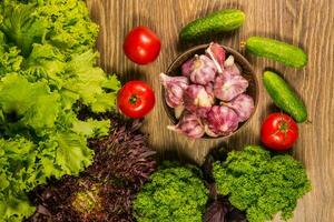 une plein bol avec Ail ampoules. tomates et concombres sur une en bois tableau. vert salade dans le Contexte. photo