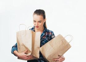 Jeune jolie fille dans bleu chemise avec plein achats Sacs dans sa mains. portrait de une content femelle avec achats Sacs isolé sur blanc Contexte. photo