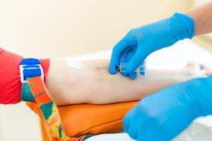 infirmière est piquer aiguille pour le seringue dans le les patients bras à prendre du sang échantillon dans une laboratoire. femme mains dans protecteur bleu gants fait du un injection dans une veine. fermer. photo