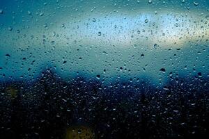 gouttes de pluie sont sur le fenêtre verre de une maison sur une bleu Contexte. fermer photo